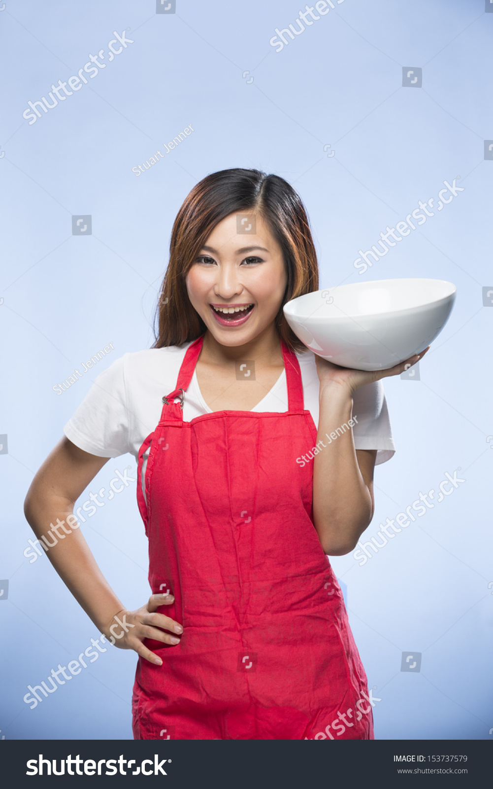 快乐的亚洲女人穿着红色的围裙,拿着碗里.